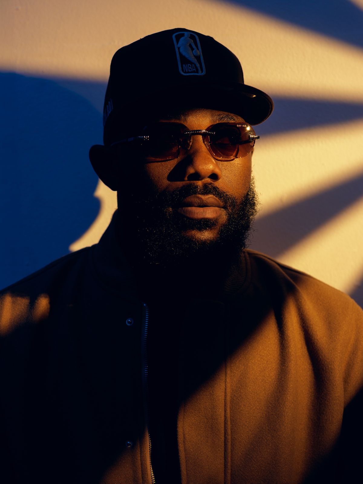 Close portrait of DJ Romie in golden light wearing sunglasses and an NBA cap
